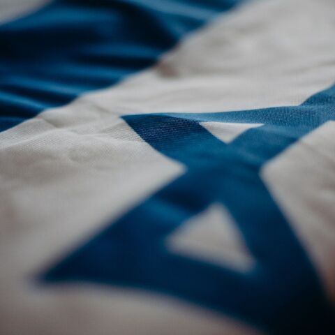 Flagge Israels Eine blau-weiß-gestreifte Flagge, auf der ein Davidstern in blauer Farbe hinterlegt ist.